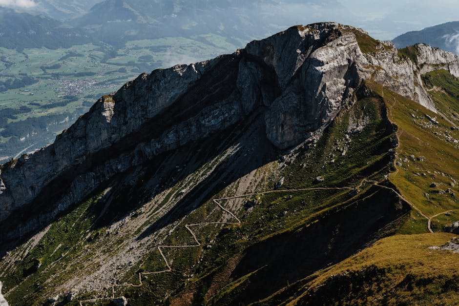 Stunning aerial view of a majestic mountain range with winding trails under a bright sky.